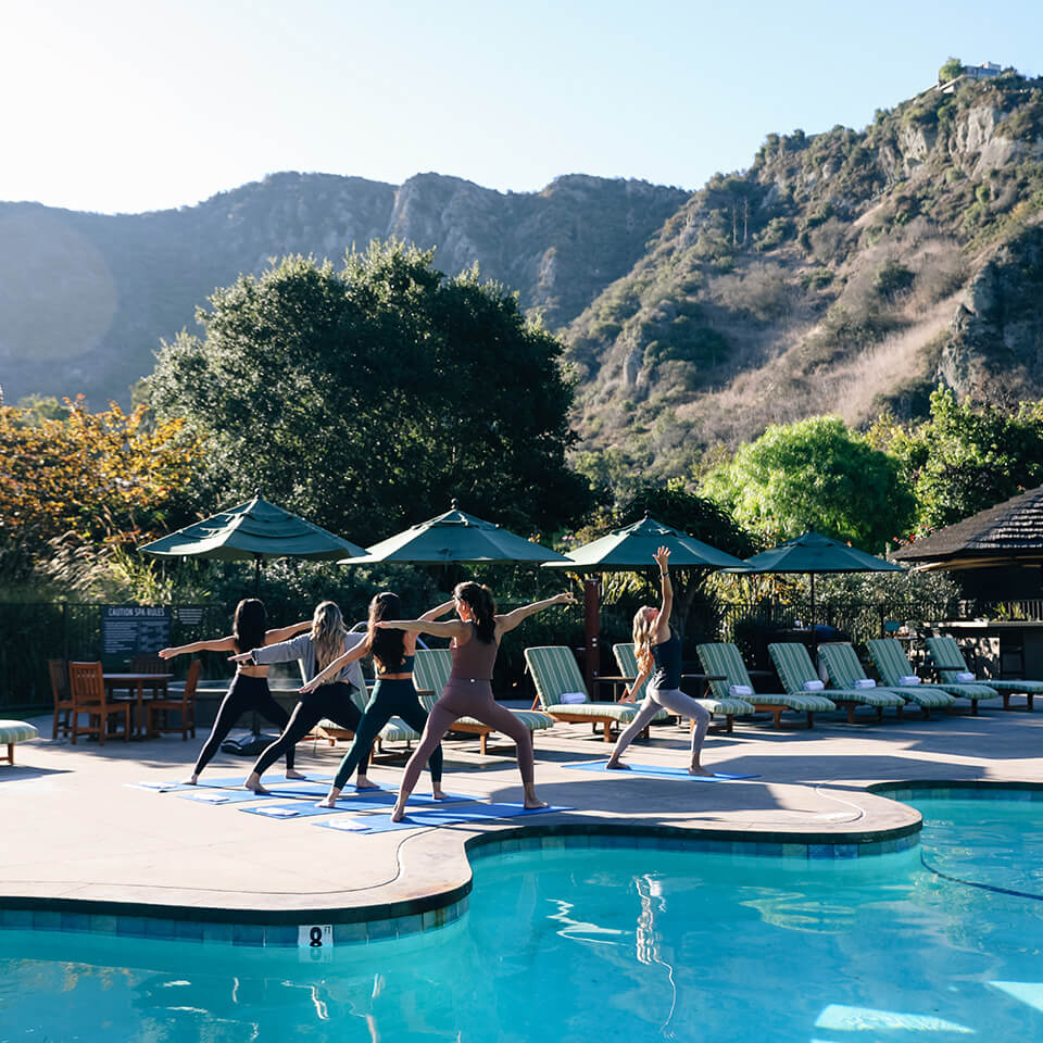 Women doing yoga by the pool