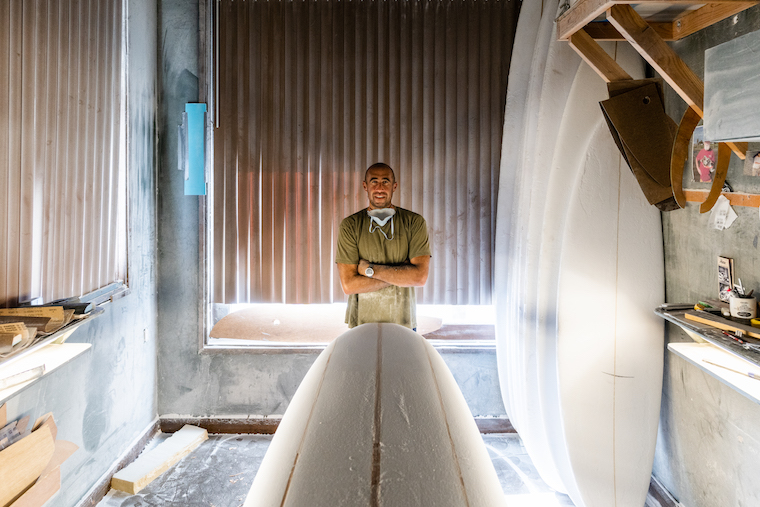 Gary Larson standing in workshop with foam surfboard